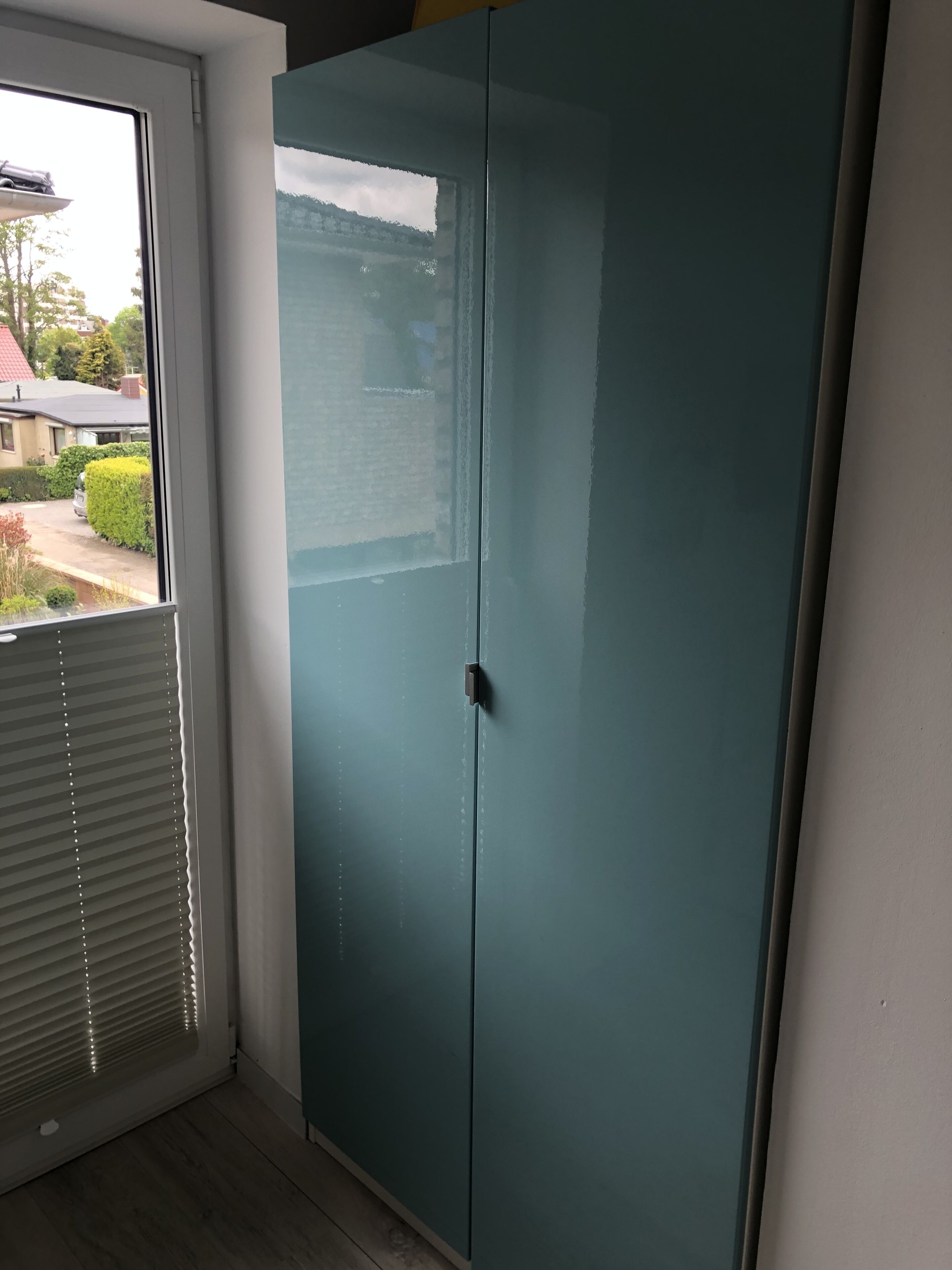 A teal-colored wardrobe in a room with a window and blinds.