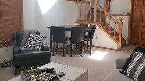 A spacious living room with a black leather sofa, a grey sofa, and a dining area with a table and chairs. A wooden staircase with a railing is visible in the background. - 2 Bedroom, 2 bath townhouse in The Galena Territory. (Galena)