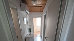 A narrow hallway with wooden ceiling beams, white walls, and a small potted plant on a white cabinet. - Apartment Bee near Bled (Zabreznica)