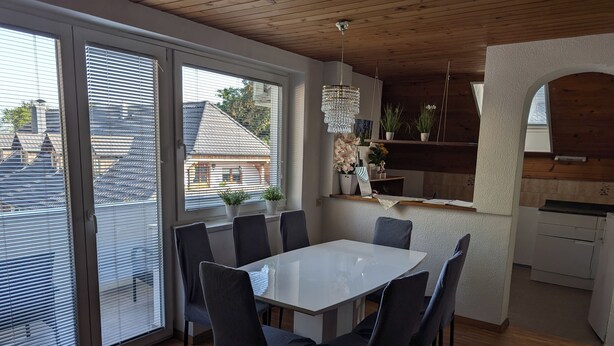 A modern dining area with a white table and dark chairs, large windows with blinds, a wooden ceiling, and a hanging chandelier. - Apartment Bee near Bled (Zabreznica)