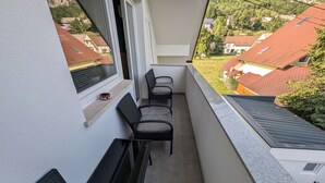 A balcony with a seating area, a window, and a view of houses. - Apartment Bee near Bled (Zabreznica)