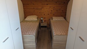 A small, cozy bedroom with two beds, wooden walls, and a nightstand with a lamp. - Apartment Bee near Bled (Zabreznica)