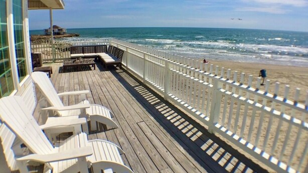 A wooden deck with white chairs and a white fence overlooking a beach. - Just Steps to the Ocean, Beachfront, House On the Beach, Minutes from Galveston (Freeport)