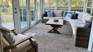 Ein Wintergarten mit einer großen Glasschiebetür, einer gepolsterten Couch, einem Holztisch und einem Korbstuhl.