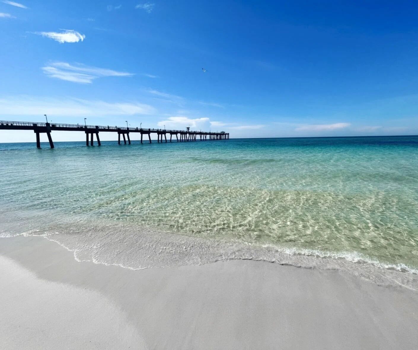 Een strand met helder ondiep water en een steiger die in zee reikt.