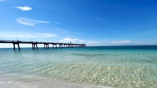 Ein Strand mit klarem, flachen Wasser und einem Steg, der ins Meer hinausführt.