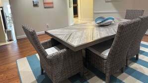 Ein Essbereich mit einem Holztisch und Korbstühlen, einem blau-weiß gestreiften Teppich und Wandbildern mit Landschaftsmotiven und Möwen.