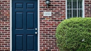 A brick house with a dark blue front door, a small window with a grid pattern, and a mailbox with the number 1106.