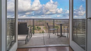 Un balcón con vistas al cielo y nubes, una parrilla y mobiliario exterior.