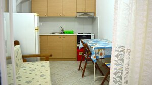 A compact kitchen with wooden cabinets, a sink, a stove, and a dining area with a table and chairs. - Apartment Danai is situated near the Centre of Ermoupolis (Ano Siros)