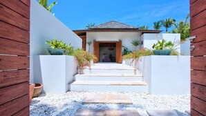 A modern house with a white exterior, a wooden entrance, and steps leading to the door. - Baan Apsara (Koh Samui)