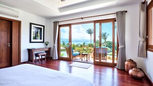 A spacious bedroom with a large bed, a desk, and a view of the outdoors through a sliding glass door. - Baan Apsara (Koh Samui)