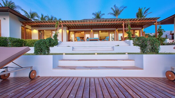 A modern house with a wooden deck, steps leading to a covered outdoor area, and palm trees in the background. - Baan Apsara (Koh Samui)