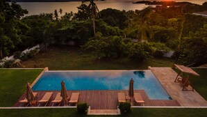 A swimming pool with lounge chairs and umbrellas, surrounded by greenery and a view of the sea at sunset. - Baan Apsara (Koh Samui)