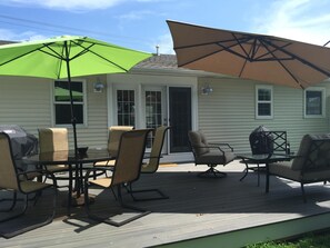 Eine Terrasse mit Gartenmöbeln, darunter Stühle und ein Tisch, sowie zwei große Sonnenschirme, die Schatten spenden.