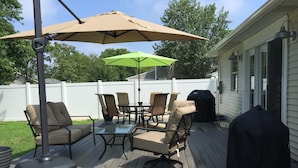 Een terras buiten met een tafel, stoelen, een barbecue en parasols.