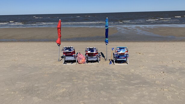 Een strand met vijf ligstoelen en twee parasols.