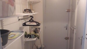 A small, narrow hallway with a door at the end, shelves with various items, and a vacuum cleaner on the floor. - Homerez - Apartment – Métabief (Métabief)