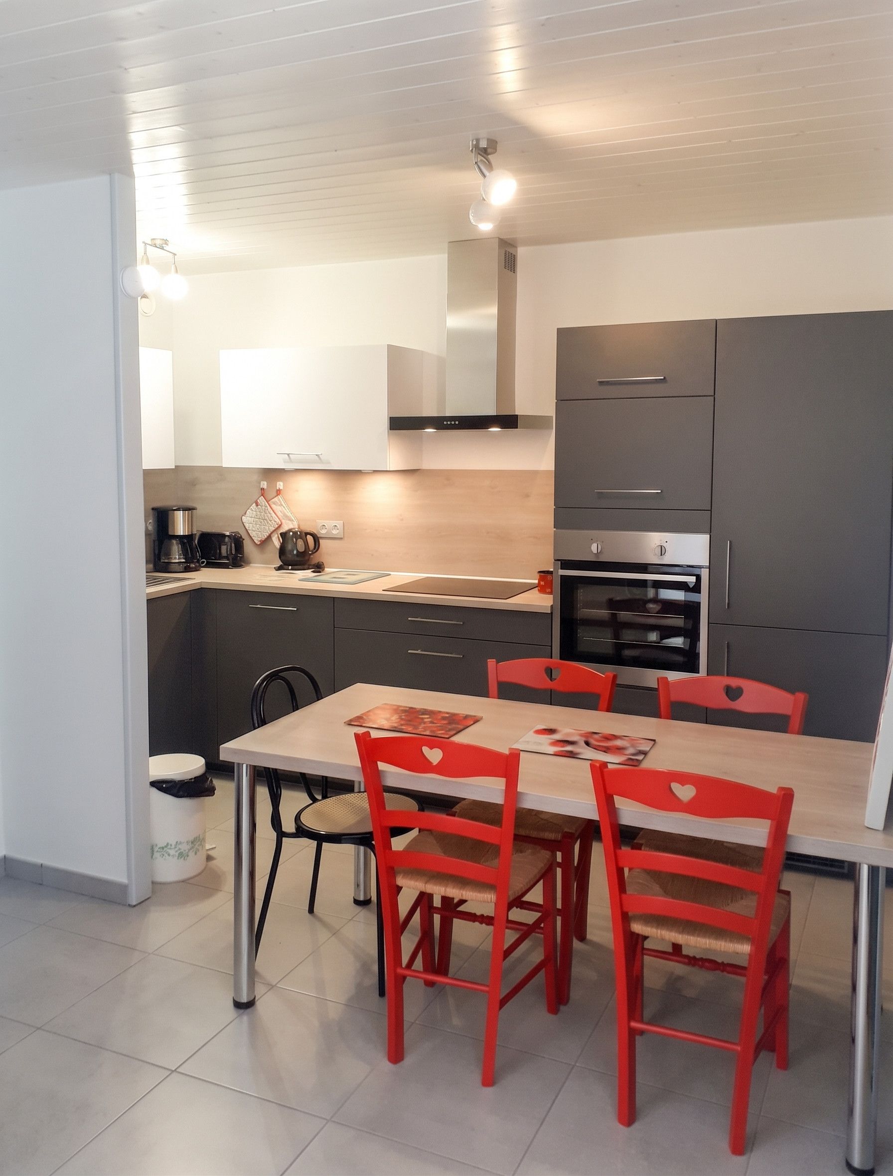 Eine moderne Küche mit grauen Schränken, einem Edelstahlbackofen und einem Esstisch mit roten Stühlen.