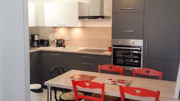 Eine moderne Küche mit grauen Schränken, einem Edelstahlbackofen und einem Esstisch mit roten Stühlen.