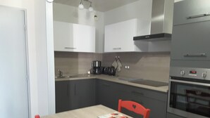 A modern kitchen with grey cabinets, a stainless steel oven, and a dining table with red chairs. - Homerez - Apartment – Métabief (Métabief)