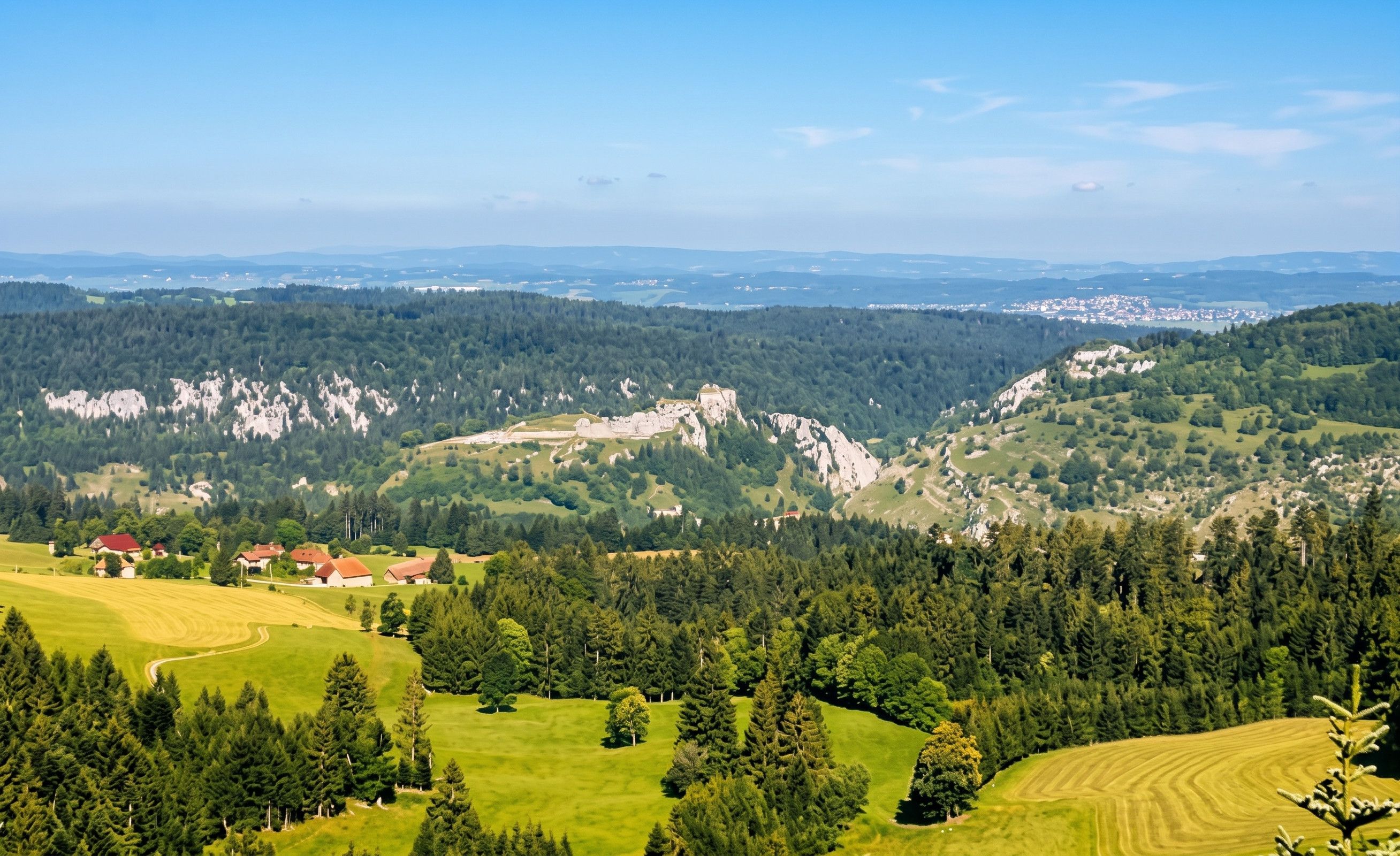 Una vista panoramica su un paesaggio montuoso con un villaggio, campi verdi e un castello.