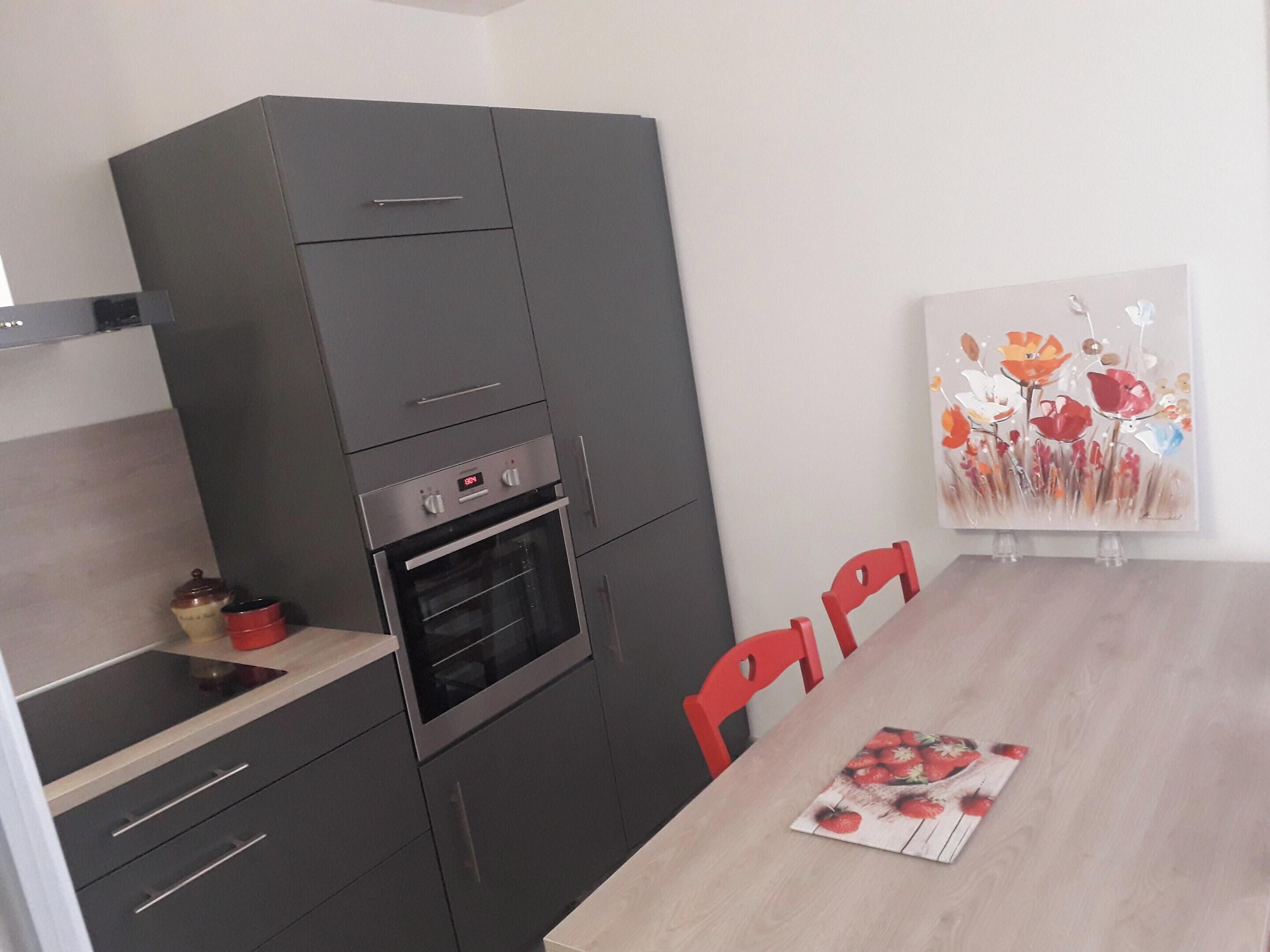 Une cuisine compacte dotée d’un four encastré, d’une table à manger avec des chaises et d’un tableau accroché au mur.