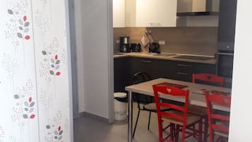 Ein kompakter Wohnraum mit Küchenzeile, einem Essbereich mit roten Stühlen und einem gemusterten Vorhang.