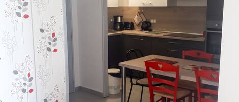 Un espacio habitable compacto con kitchenette, una zona de comedor con sillas rojas y una cortina estampada.