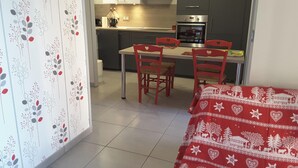 A small, modern kitchen with a dining area, featuring a table and chairs, and a bed with a red and white patterned bedspread. - Homerez - Apartment – Métabief (Métabief)