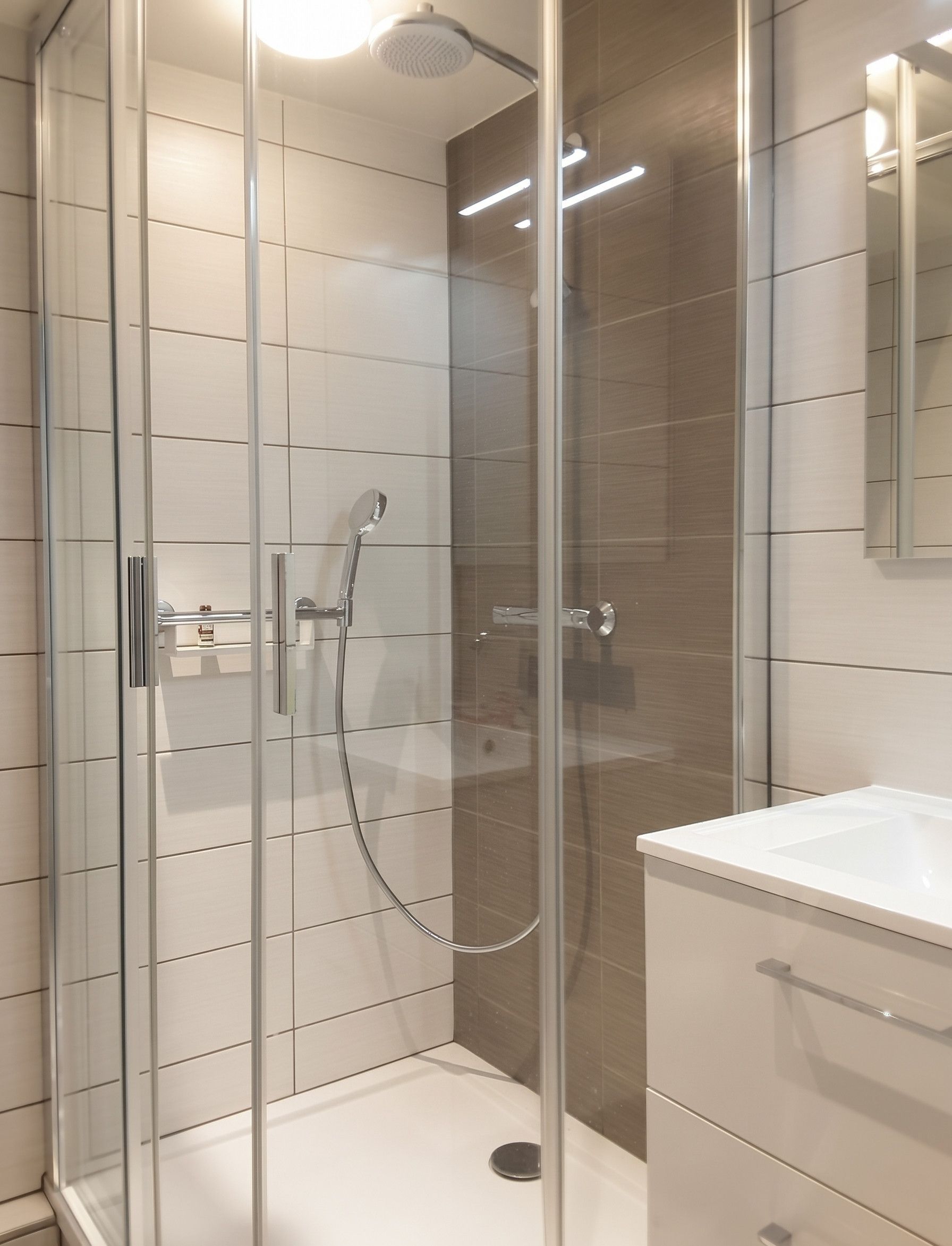 A modern shower enclosure with a glass door, a handheld showerhead, and a wall-mounted control panel.