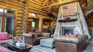 A log cabin interior with a stone fireplace, leather sofas, and a staircase leading to an upper level. - Limber Pine Lodge by Cottonwood Lodging (Brighton)