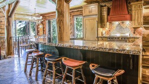 A rustic kitchen with wooden cabinets, a granite countertop, and a large island with bar stools. - Limber Pine Lodge by Cottonwood Lodging (Brighton)