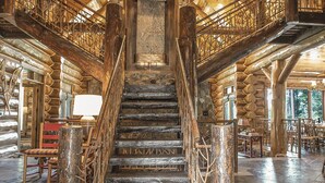 A log cabin interior with a central staircase, wooden railings, and rustic decor. - Limber Pine Lodge by Cottonwood Lodging (Brighton)
