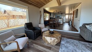 Un vaste espace de vie doté d’un plafond en bois, un coin repas avec une cuisine en arrière-plan, et une vue sur l’extérieur.