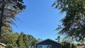 Une maison moderne à l’extérieur sombre, avec un escalier en pierre menant à la porte d’entrée, et un ciel bleu clair en arrière-plan.