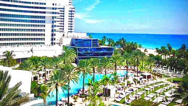 A resort with a large pool area, palm trees, and a view of the ocean.