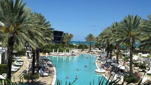 A resort pool area with palm trees, lounge chairs, and boats.