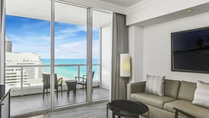A hotel room with a balcony, a sofa, a table, and a lamp.