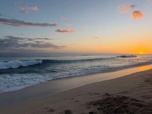 A beach with waves, a sunset, and footprints in the sand. - Panoramic Ocean/Mountain View Apartment  (Mākaha)