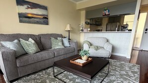 A living room with a gray sofa, a coffee table, and a patterned rug. - Panoramic Ocean/Mountain View Apartment  (Mākaha)