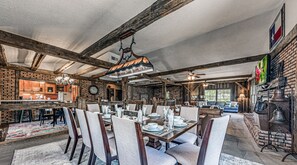 Un coin repas rustique avec des poutres apparentes, un mur en briques et une grande table à manger dressée pour six personnes.