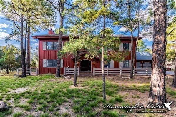 Une cabane rouge avec un porche blanc, entourée d’arbres et d’herbe.