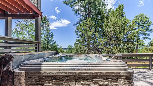 Un jacuzzi en una terraza de madera con vistas a árboles y un cielo despejado.