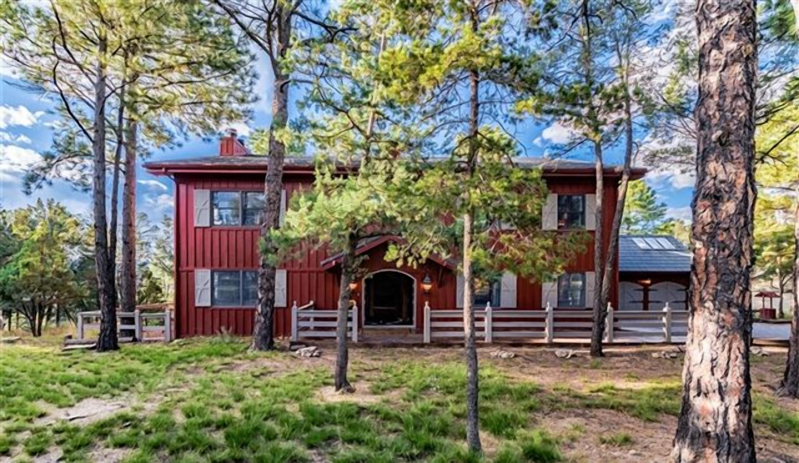 A red cabin with a white porch, surrounded by trees and grass.