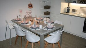Een eettafel gedekt met borden, glazen en bestek, omringd door witte stoelen met houten poten.