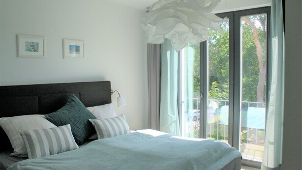 Een slaapkamer met een groot bed, een hoofdbord, twee ingelijste foto’s aan de muur en een uitzicht op het omliggende landschap door het raam.