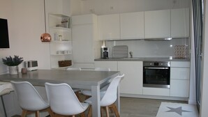 Een moderne keuken met witte kasten, een roestvrijstalen oven en een eetgedeelte met witte stoelen.