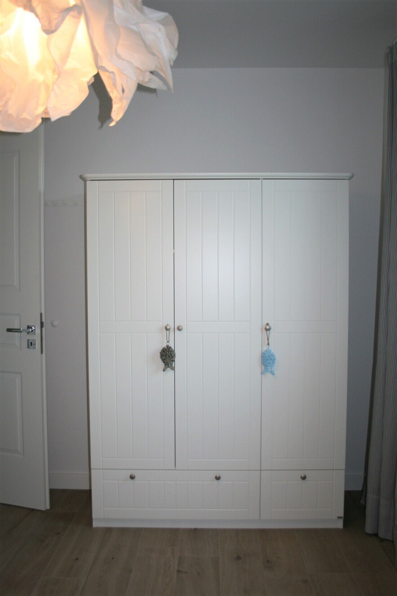 Un armario blanco con dos puertas y un cajón pequeño, un tirador de puerta y un perchero en la puerta derecha.