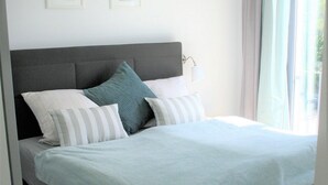 Een moderne slaapkamer met een bed, kussens, een bedlampje en een raam met gordijnen.